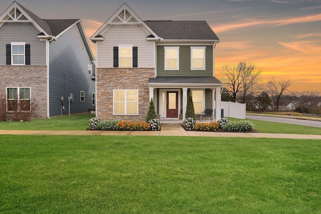 craftsman-style house featuring a front lawn, covered porch, stone siding, and a shingled roof