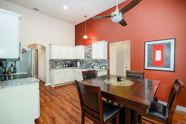 dining space with ceiling fan, visible vents, arched walkways, wood finished floors, and high vaulted ceiling