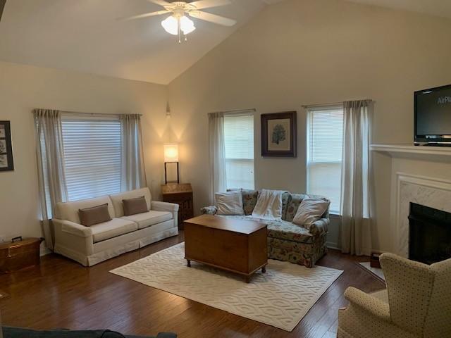 living area with high vaulted ceiling, wood finished floors, a ceiling fan, and a high end fireplace