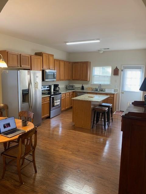 kitchen featuring brown cabinets, appliances with stainless steel finishes, a kitchen island, light countertops, and dark wood-style floors