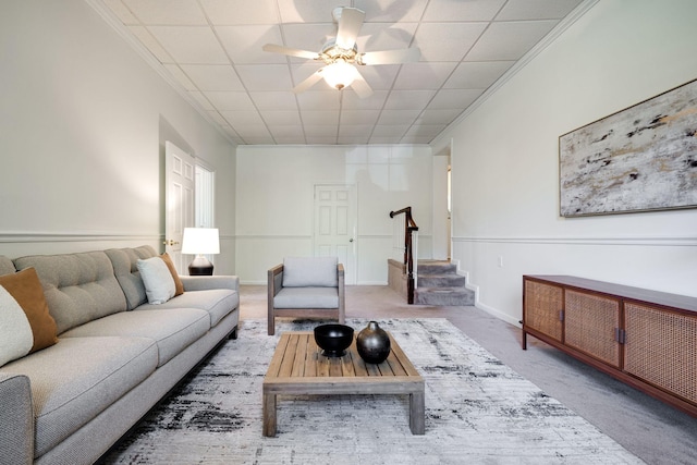 carpeted living area featuring baseboards, ceiling fan, and stairs