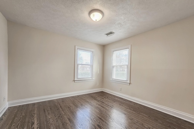 empty room with a textured ceiling, visible vents, dark wood-type flooring, and baseboards