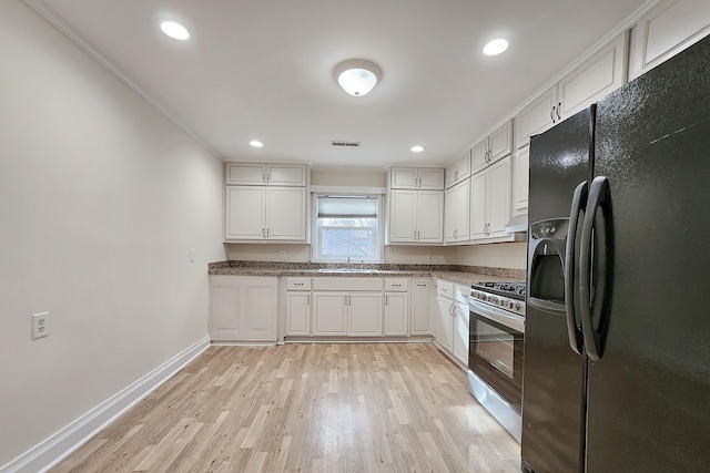 kitchen with a sink, light wood-style floors, black fridge, visible vents, and stainless steel gas stove
