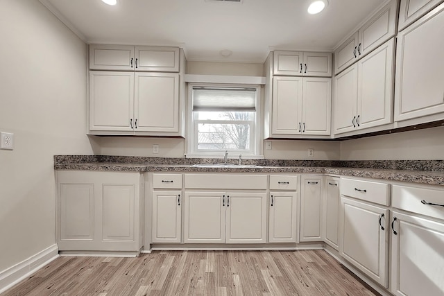 kitchen featuring white cabinets, a sink, dark countertops, recessed lighting, and light wood finished floors