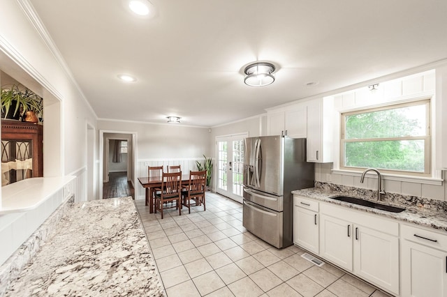 kitchen featuring visible vents, a sink, stainless steel fridge, ornamental molding, and white cabinetry