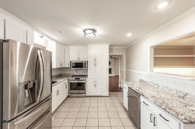 kitchen with white cabinets, light tile patterned flooring, a wainscoted wall, stainless steel appliances, and ornamental molding