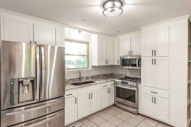 kitchen with white cabinets, appliances with stainless steel finishes, light stone counters, a sink, and light tile patterned floors