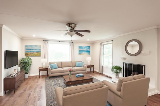 living room featuring crown molding, a ceiling fan, light wood finished floors, and baseboards
