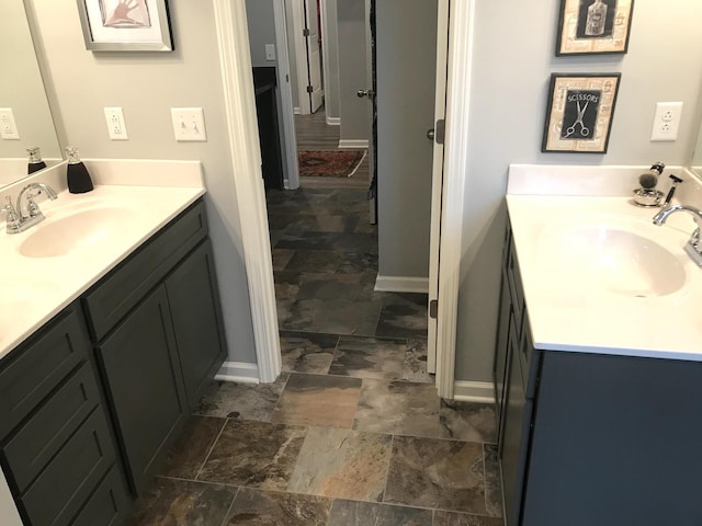 bathroom featuring two vanities, a sink, stone tile flooring, and baseboards