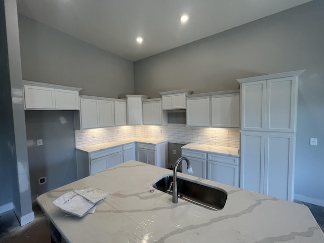 kitchen with tasteful backsplash, white cabinets, a sink, baseboards, and high vaulted ceiling