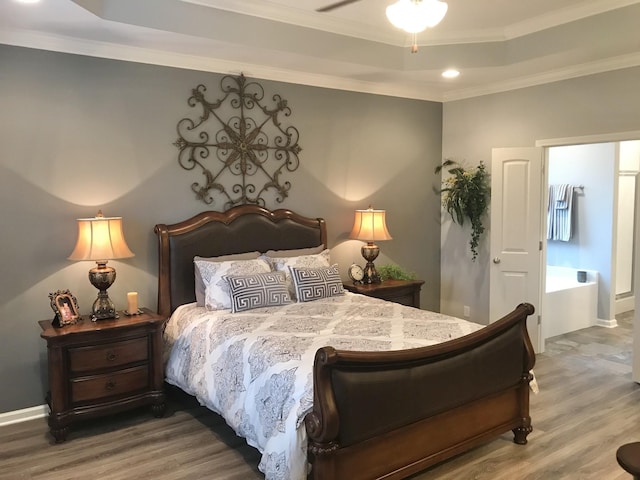 bedroom featuring baseboards, wood finished floors, ornamental molding, and a tray ceiling
