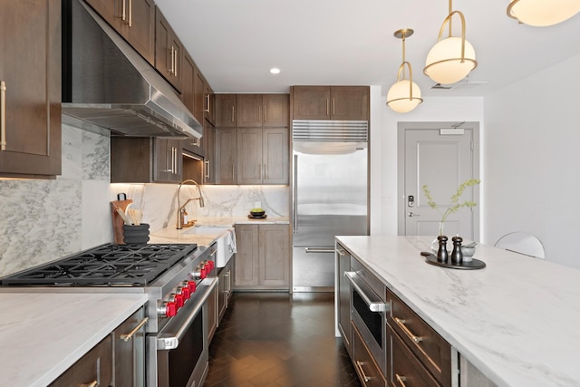 kitchen featuring light stone counters, a sink, high end appliances, decorative backsplash, and under cabinet range hood