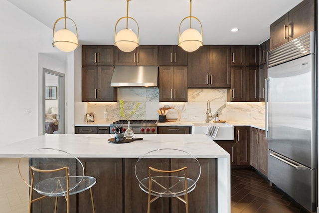 kitchen featuring dark brown cabinets, built in refrigerator, ventilation hood, a sink, and range