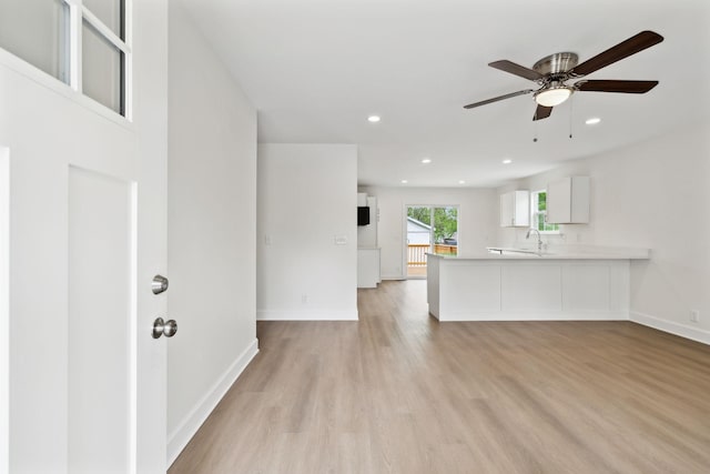 unfurnished living room featuring a ceiling fan, a sink, light wood-style flooring, and baseboards