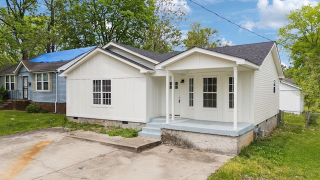 view of front of house with board and batten siding, a shingled roof, a front yard, crawl space, and a porch