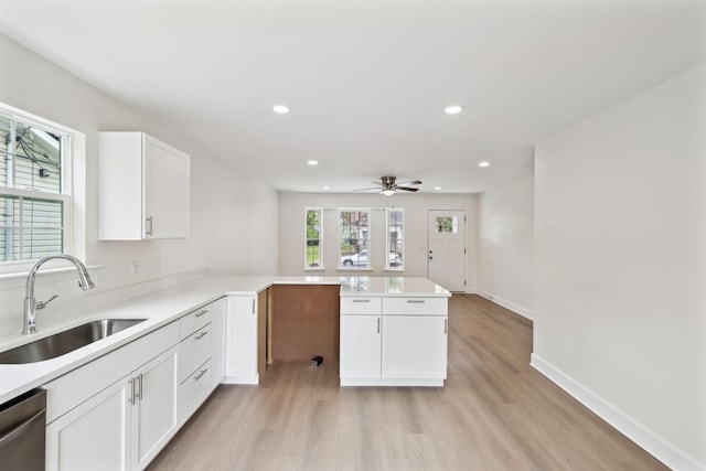 kitchen featuring white cabinetry, light wood-style flooring, a sink, dishwasher, and a peninsula