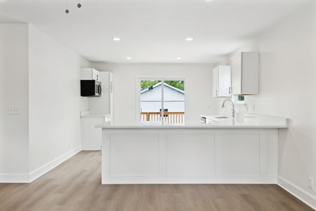 kitchen featuring white cabinetry, light wood-style flooring, light countertops, a sink, and baseboards