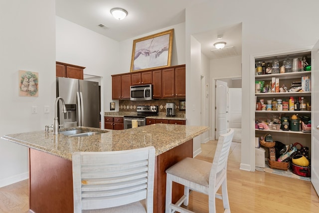 kitchen with stainless steel appliances, a breakfast bar, light stone countertops, and light wood-style flooring