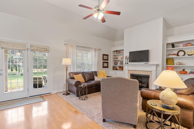 living area with a fireplace, built in shelves, vaulted ceiling, a ceiling fan, and healthy amount of natural light