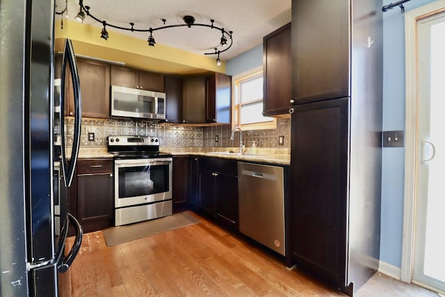 kitchen featuring backsplash, dark brown cabinets, appliances with stainless steel finishes, and light wood-style floors