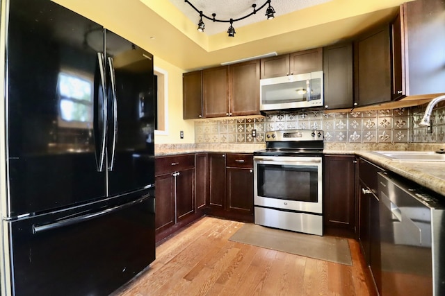 kitchen with a sink, decorative backsplash, light wood-type flooring, track lighting, and appliances with stainless steel finishes