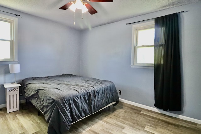 bedroom featuring a ceiling fan, a textured ceiling, wood finished floors, and baseboards