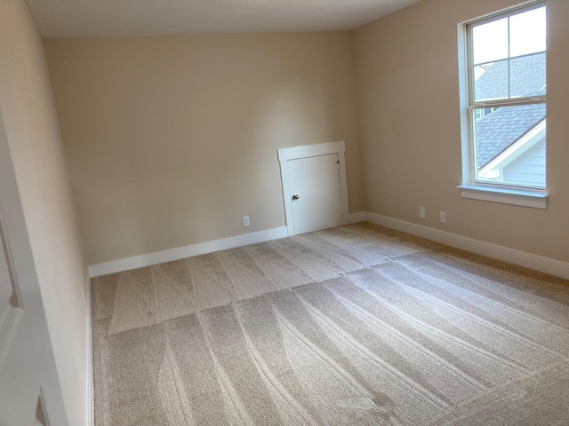 spare room with baseboards and light colored carpet