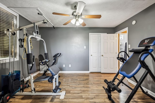 exercise area with attic access, a textured ceiling, wood finished floors, and ceiling fan