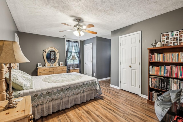bedroom featuring a textured ceiling, two closets, baseboards, wood finished floors, and a ceiling fan