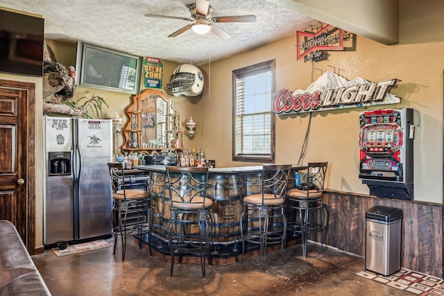 bar featuring stainless steel fridge with ice dispenser, finished concrete floors, a ceiling fan, a textured ceiling, and a dry bar