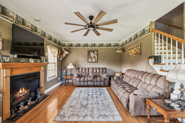 living room featuring stairway, ceiling fan, hardwood / wood-style floors, a lit fireplace, and baseboards