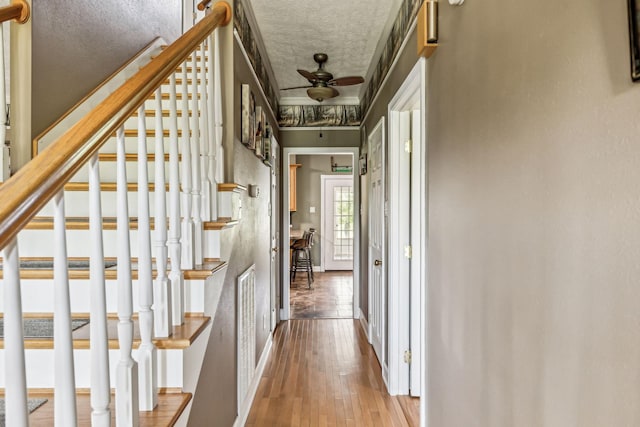 corridor with a textured ceiling, hardwood / wood-style floors, stairs, and baseboards