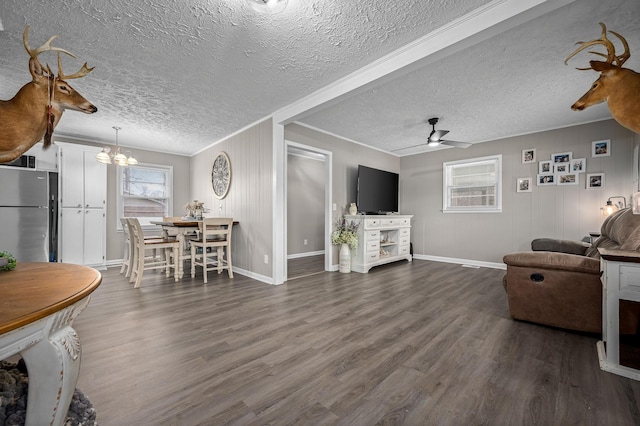 living area with ornamental molding, dark wood-style flooring, a wealth of natural light, and ceiling fan with notable chandelier