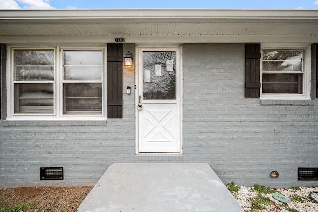 view of exterior entry with brick siding and crawl space