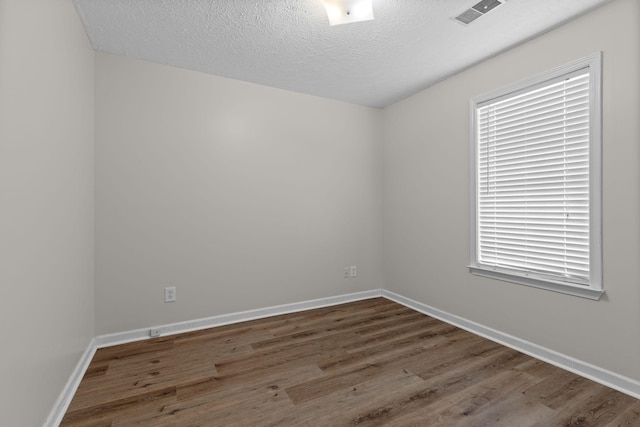 spare room featuring baseboards, visible vents, wood finished floors, and a textured ceiling