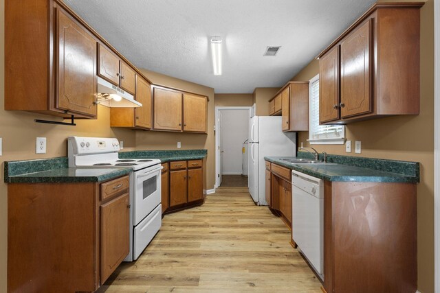 kitchen with white appliances, light wood-style floors, under cabinet range hood, a sink, and visible vents