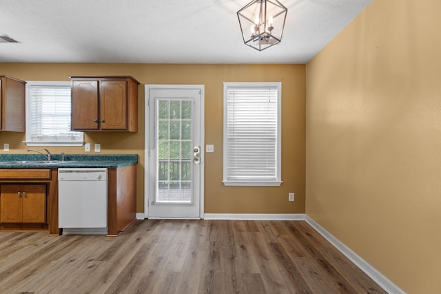 kitchen featuring light wood-style flooring, brown cabinetry, white dishwasher, dark countertops, and a sink