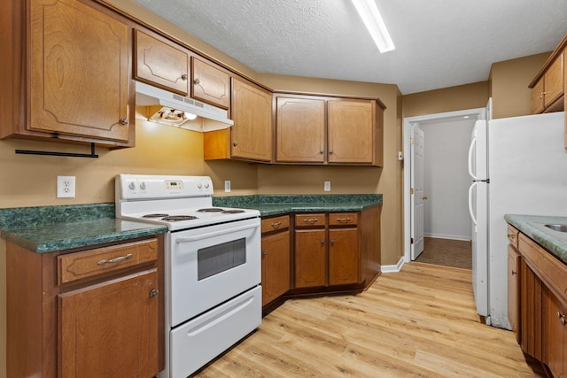 kitchen with light wood-type flooring, dark countertops, under cabinet range hood, and white appliances