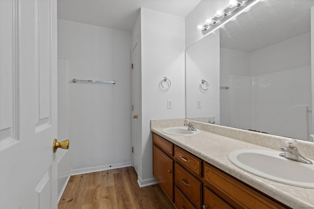 bathroom featuring baseboards, wood finished floors, double vanity, and a sink