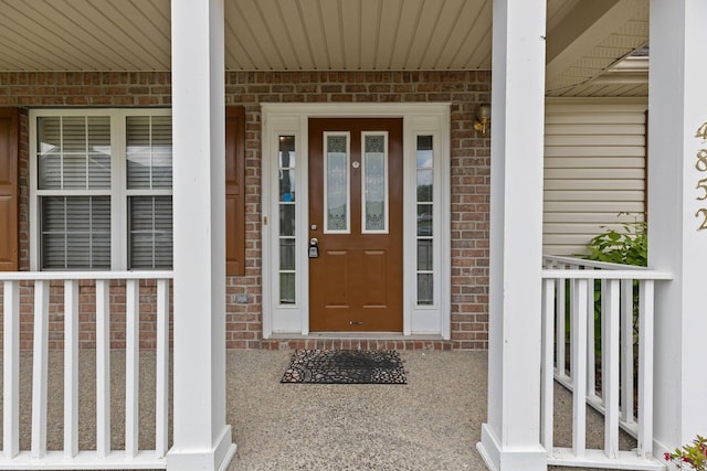 entrance to property with a porch and brick siding