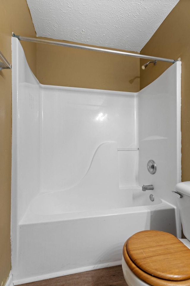 full bath with a textured ceiling, shower / washtub combination, toilet, and wood finished floors
