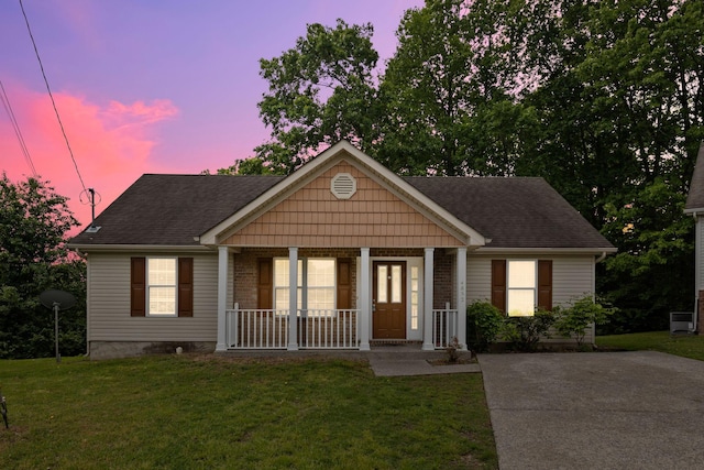 view of front of house featuring covered porch, driveway, a yard, and roof with shingles