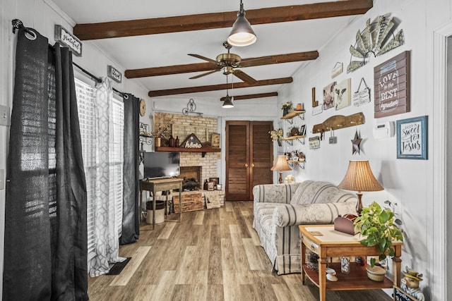 living area with beam ceiling, wood finished floors, ceiling fan, and a brick fireplace