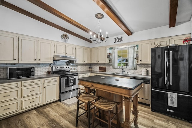 kitchen with tasteful backsplash, a sink, appliances with stainless steel finishes, under cabinet range hood, and cream cabinetry