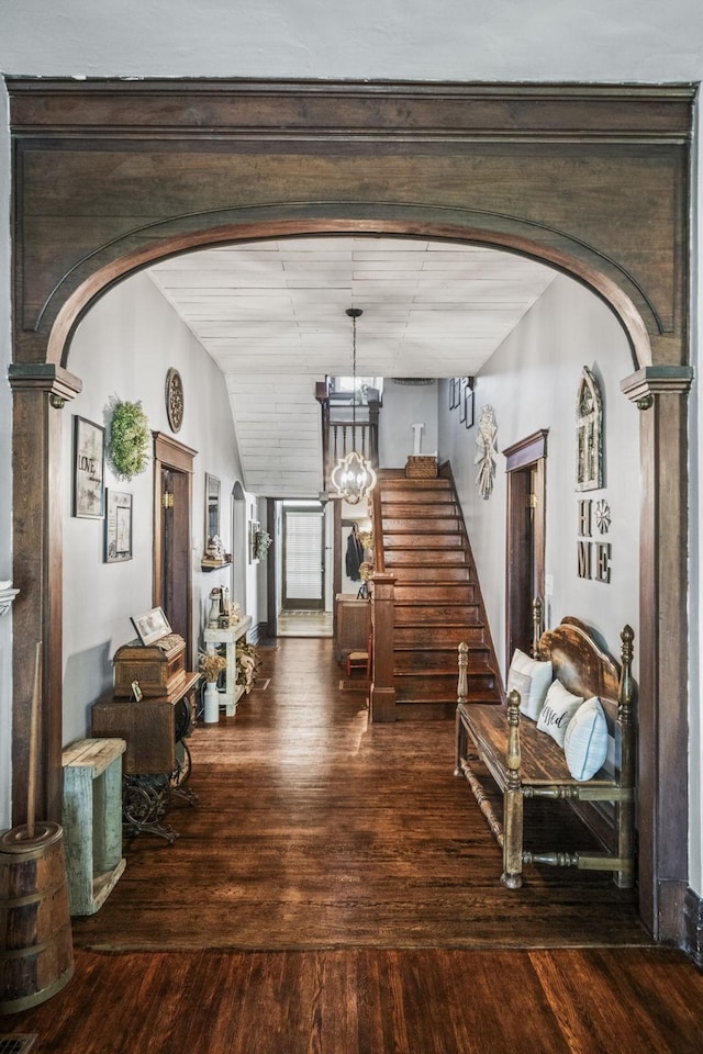 hall with hardwood / wood-style floors, stairway, arched walkways, and an inviting chandelier