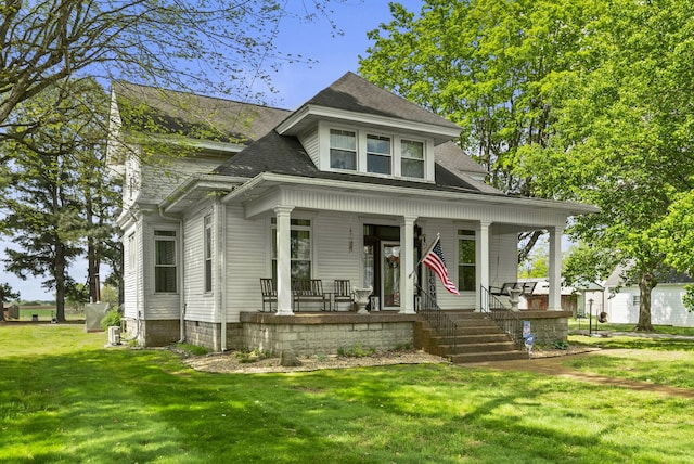 view of front of property with covered porch, a shingled roof, and a front yard