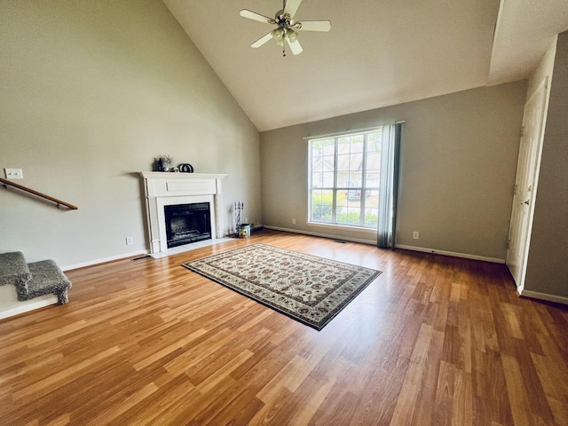 unfurnished living room with a fireplace with flush hearth, ceiling fan, baseboards, wood finished floors, and high vaulted ceiling