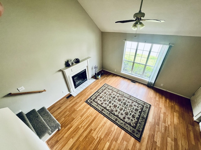 unfurnished living room featuring a tiled fireplace, wood finished floors, baseboards, visible vents, and a ceiling fan