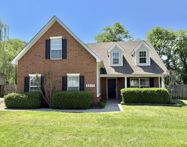 view of front of house with a front yard, fence, a shingled roof, and brick siding