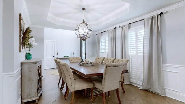 dining room with a wainscoted wall, wood finished floors, a tray ceiling, and a notable chandelier